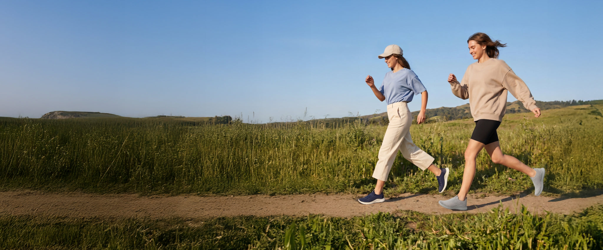 Two people running on a path in a field with a clear blue sky.