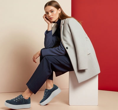 image of women in a navy outfit and taupe trench coat n navy platform sneakers on a white and red background