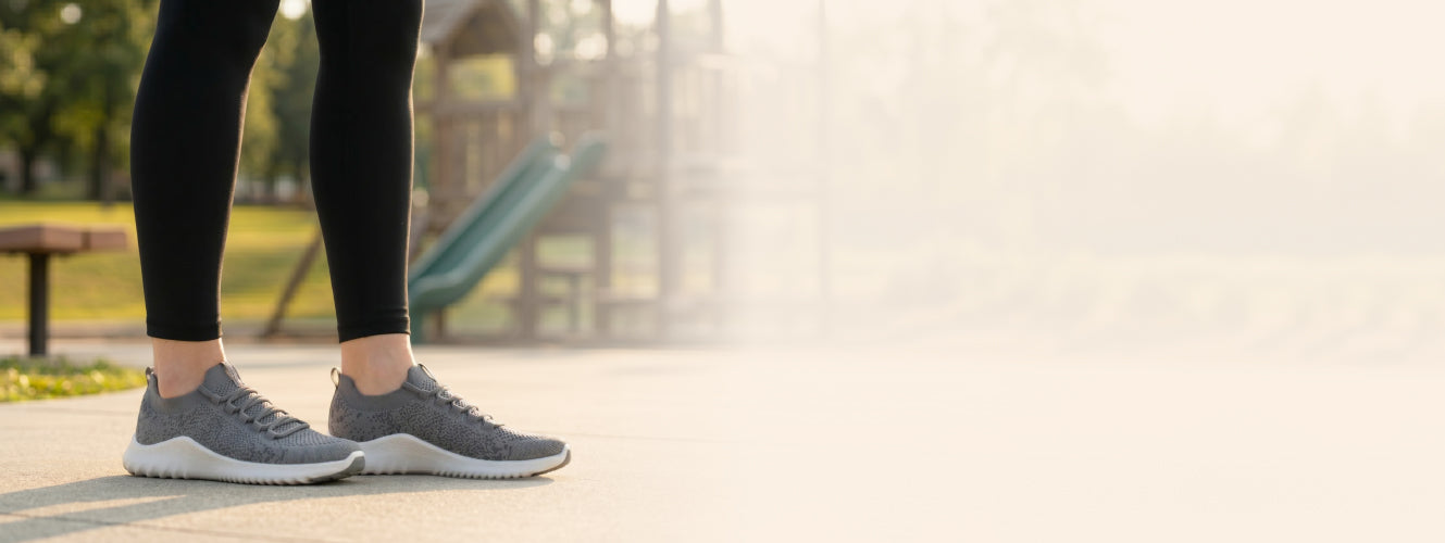 Person wearing gray sneakers and black leggings on a blurred outdoor background