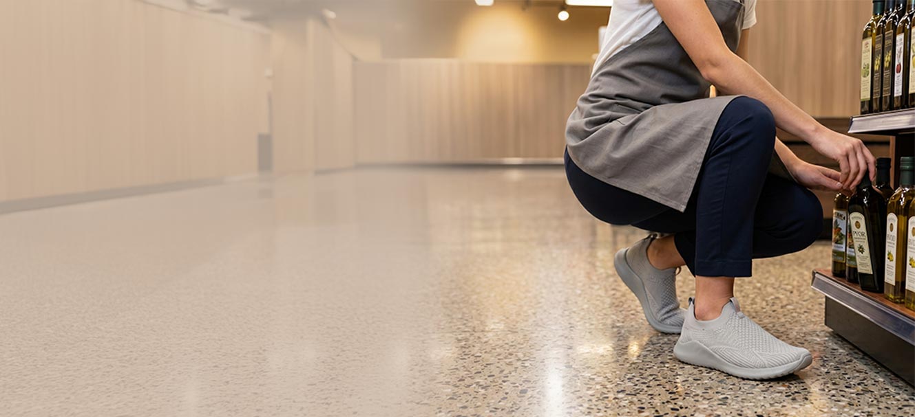 Person wearing light gray sneakers walking on a concrete floor with shelves in the background.