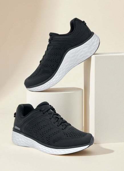 Black athletic shoes on white cylindrical blocks against a beige background