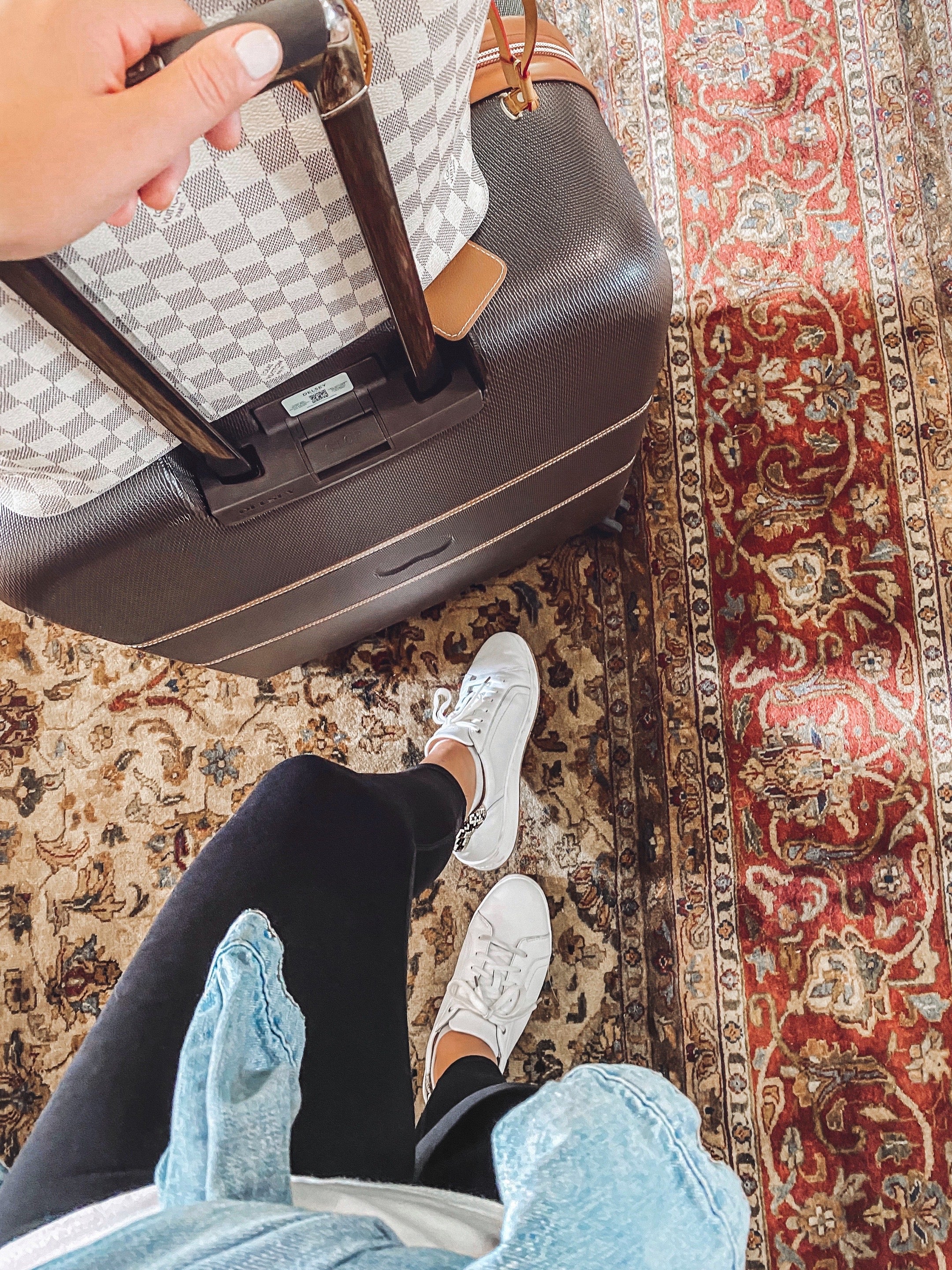 Person holding a suitcase on a patterned rug