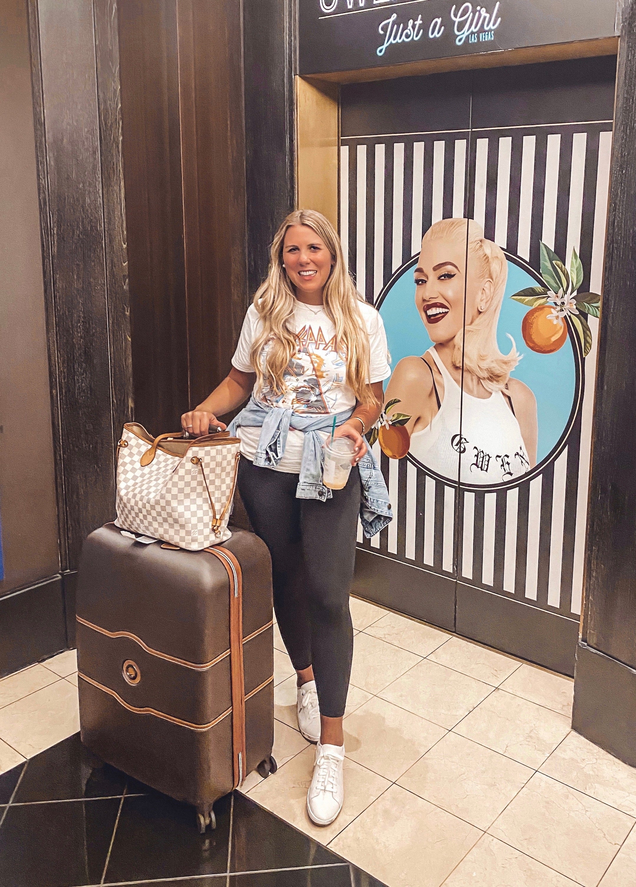 Woman with a suitcase and handbag in front of a store entrance with a decorative wall.