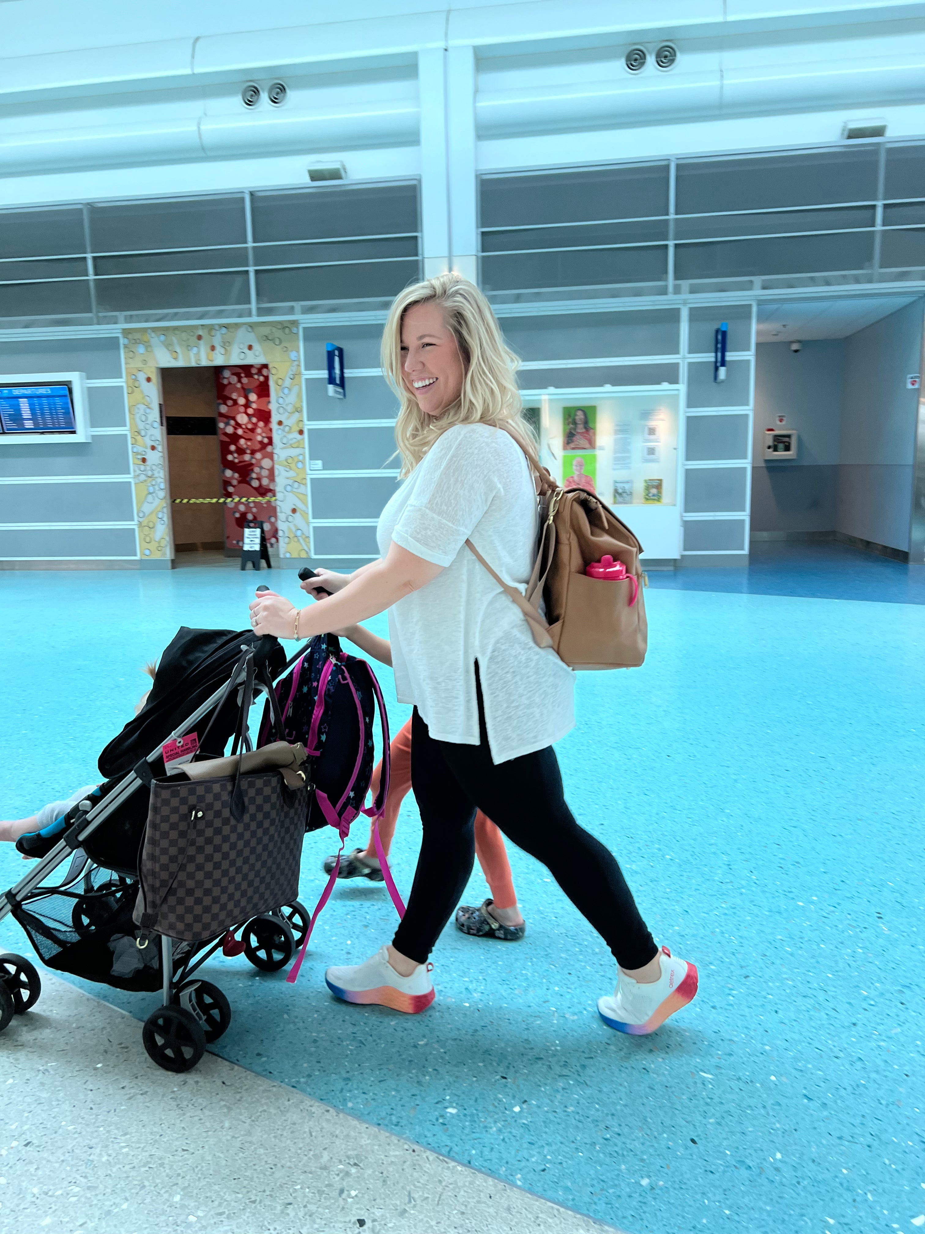 Woman pushing a stroller in an indoor setting with blue flooring and large windows.