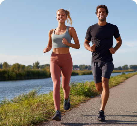 Two people jogging along a path by a river with a clear blue sky.