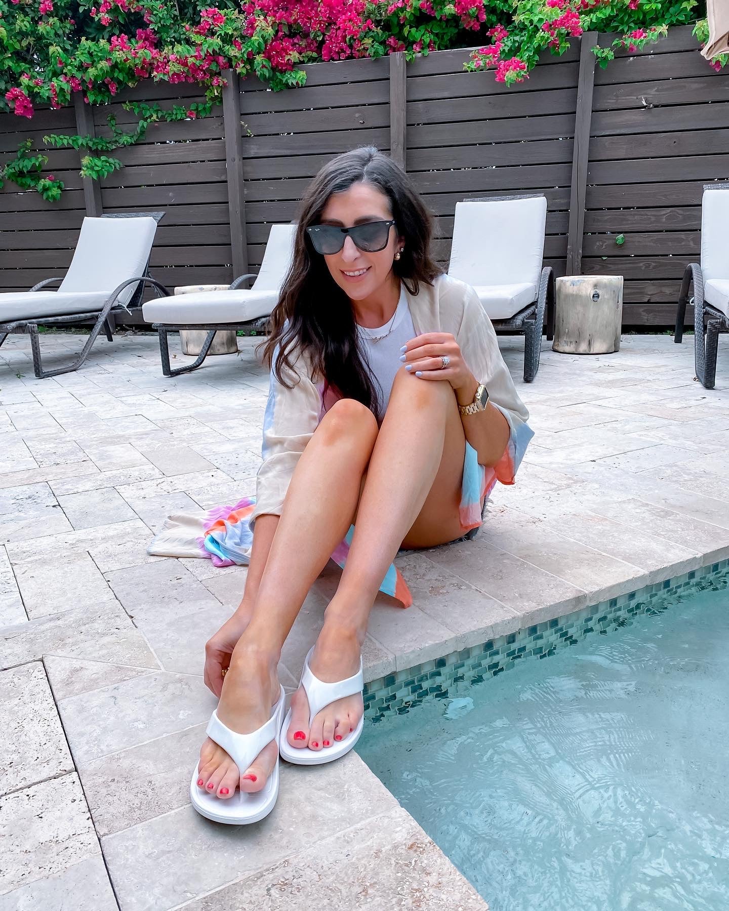 Woman sitting by a pool with sunglasses and white sandals