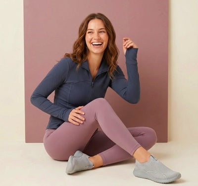Woman sitting on the floor wearing a blue long-sleeve top and pink leggings against a pink background