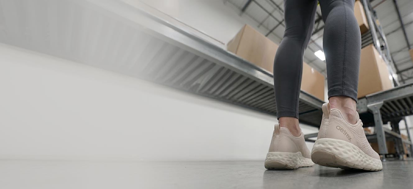Person wearing white sneakers on a tiled floor with a suitcase in the background