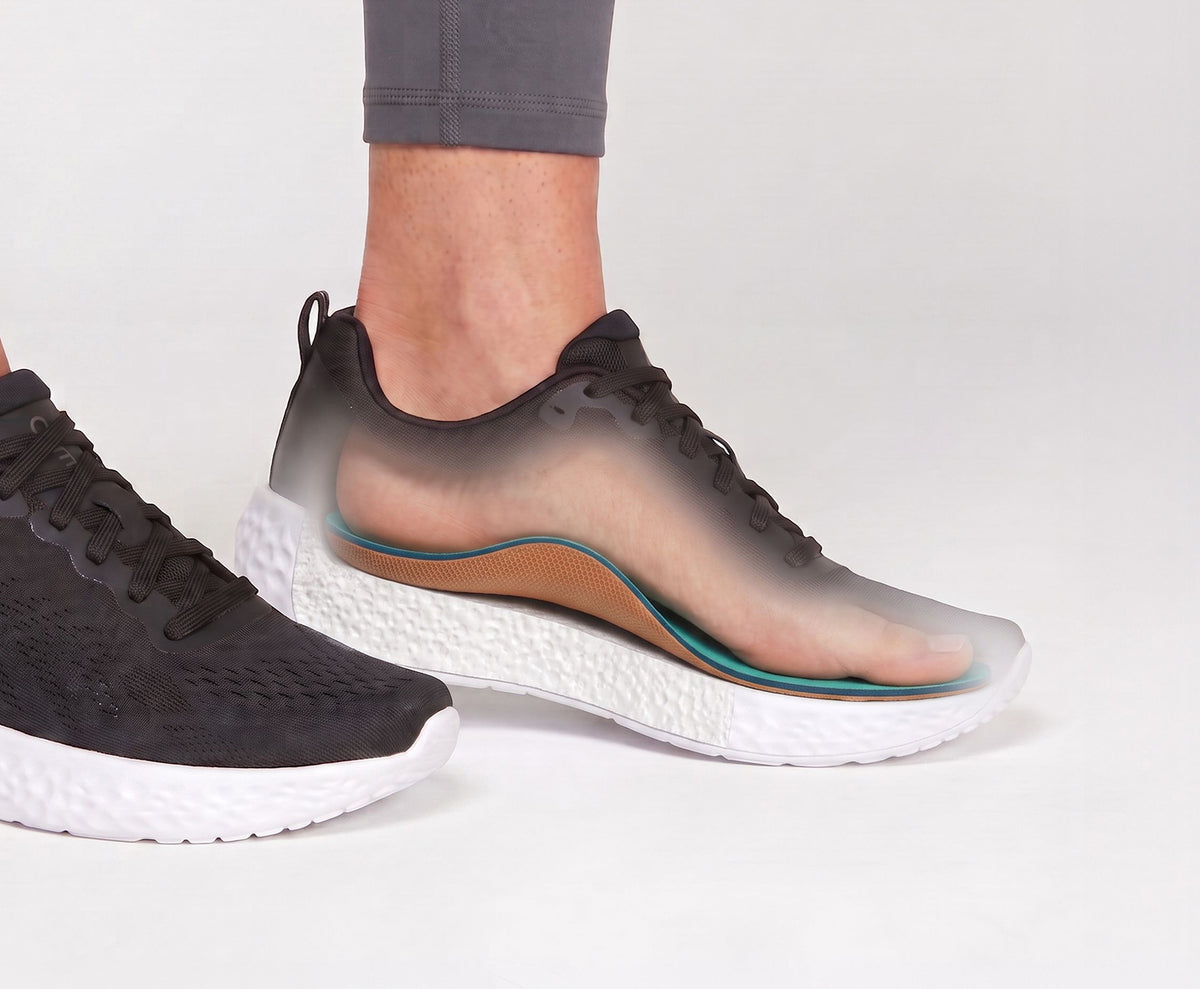 A close-up of a person's feet wearing black athletic sneakers with a translucent overlay showing the inner footbed and cushioning, set against a clean white studio background.