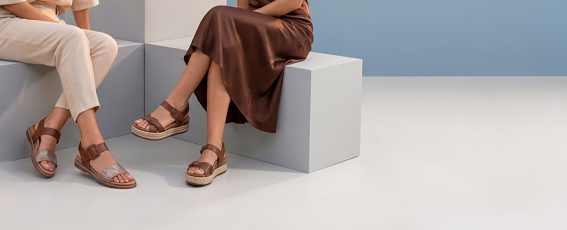 Two people sitting on a modern architectural bench wearing brown sandals.