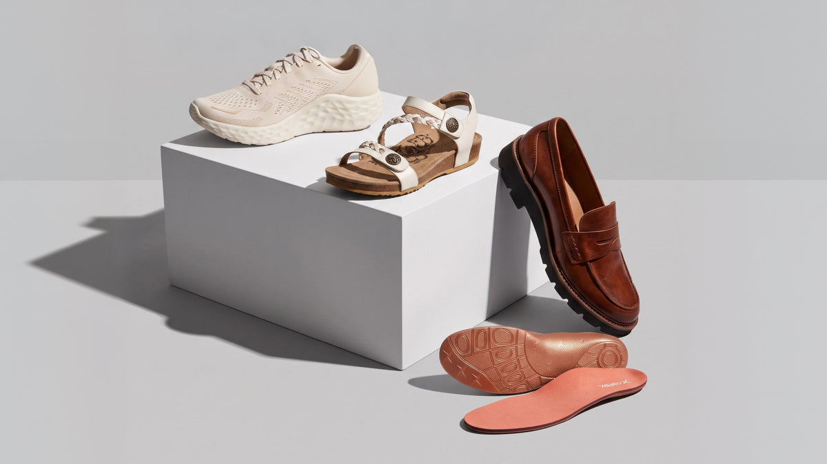 A styled product display featuring a pair of beige sneakers, brown sandals, a brown leather loafer, and two pink orthopedic insoles arranged around a white display block on a light gray background.