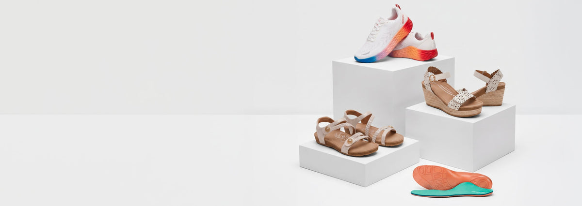 A collection of women's casual footwear displayed on white pedestals against a clean white studio background. The set includes white sneakers with red and blue accents, brown strappy sandals, and tan wedge sandals, with one tan sandal shown flat on its side in front.