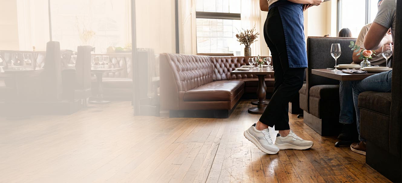 Person wearing blue sneakers on a wooden floor in a room with furniture.